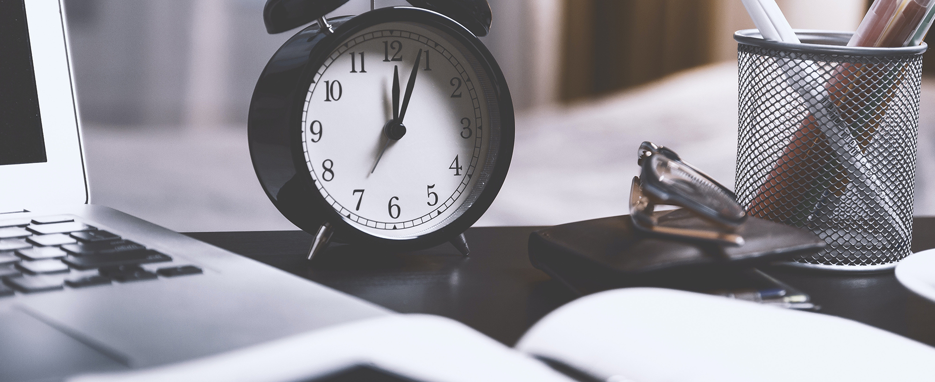 clock on desk with paperwork and laptop